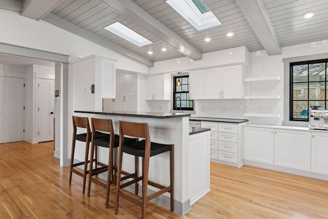 kitchen featuring a breakfast bar, light wood-type flooring, white cabinetry, open shelves, and backsplash