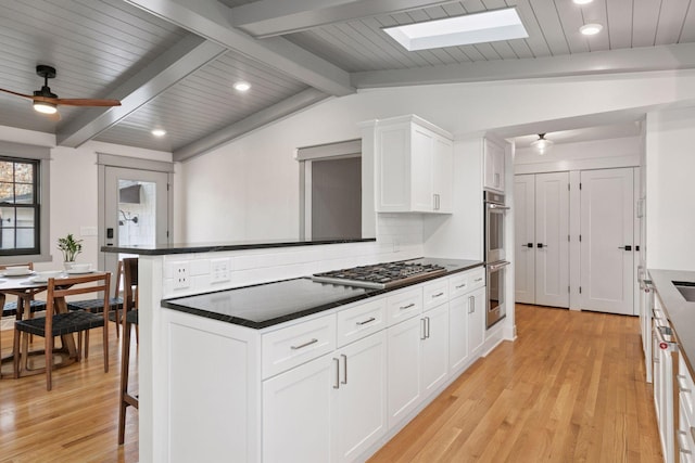 kitchen featuring stainless steel appliances, dark countertops, light wood-style flooring, backsplash, and vaulted ceiling with skylight