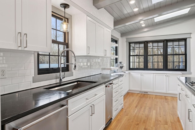 kitchen featuring decorative backsplash, lofted ceiling with beams, stainless steel dishwasher, white cabinetry, and a sink