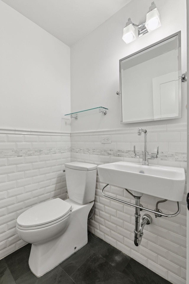 half bath featuring toilet, a wainscoted wall, a sink, tile walls, and tile patterned floors