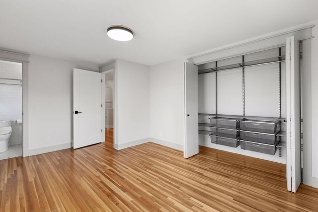 unfurnished bedroom featuring light wood finished floors, a closet, connected bathroom, and baseboards