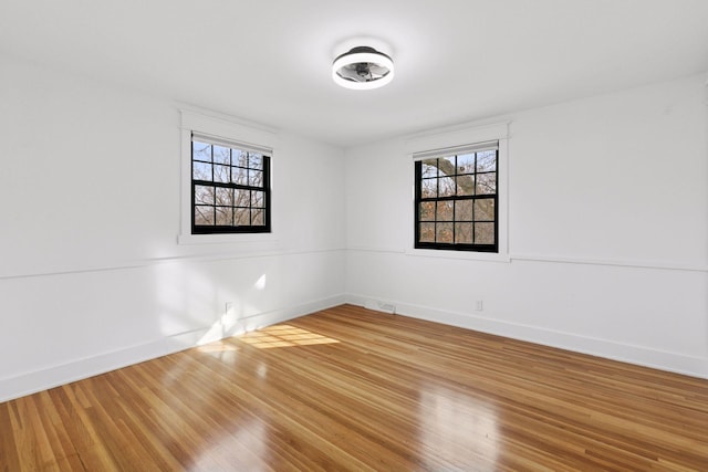 spare room with wood finished floors, visible vents, and baseboards