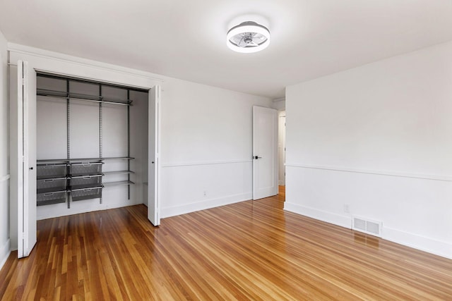 unfurnished bedroom with baseboards, a closet, visible vents, and wood finished floors