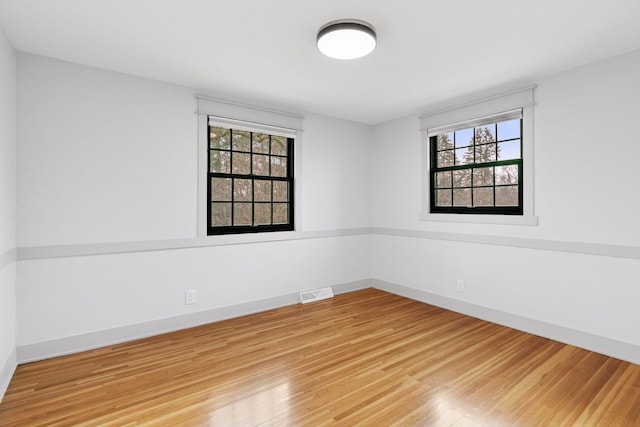 unfurnished room with wood finished floors, visible vents, and baseboards