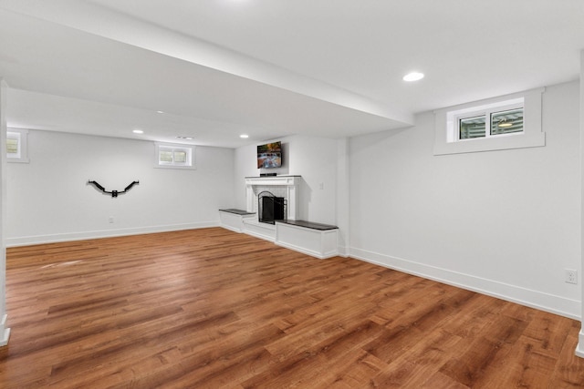 below grade area featuring baseboards, a fireplace with raised hearth, wood finished floors, and recessed lighting