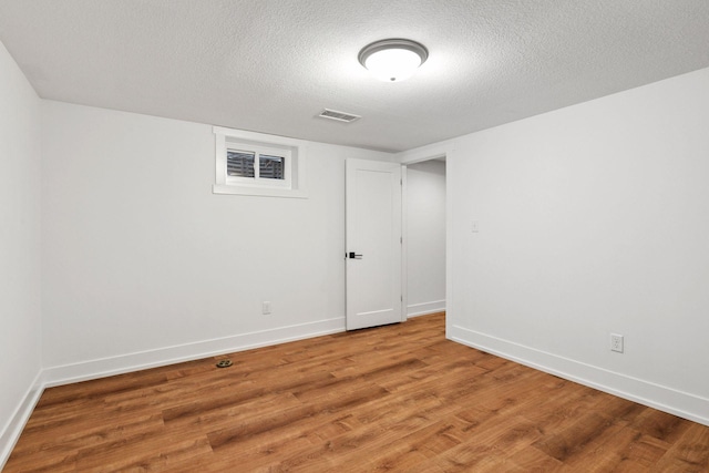 empty room featuring light wood-style flooring, a textured ceiling, visible vents, and baseboards