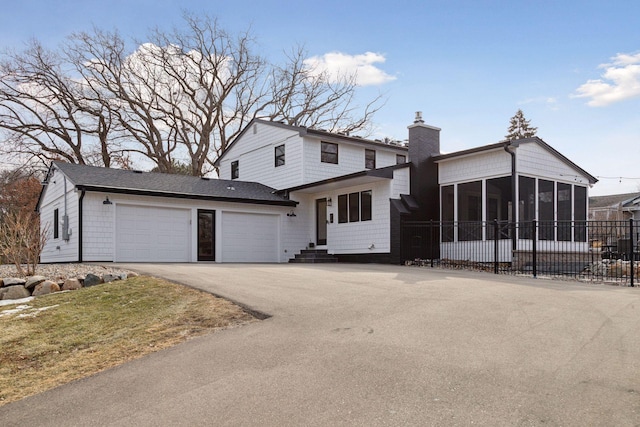 view of front of house with a chimney, a sunroom, fence, a garage, and driveway