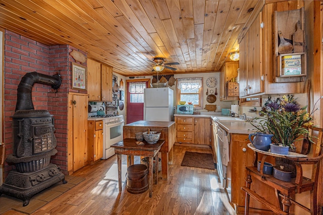 kitchen with light countertops, wooden ceiling, light wood finished floors, a wood stove, and white appliances