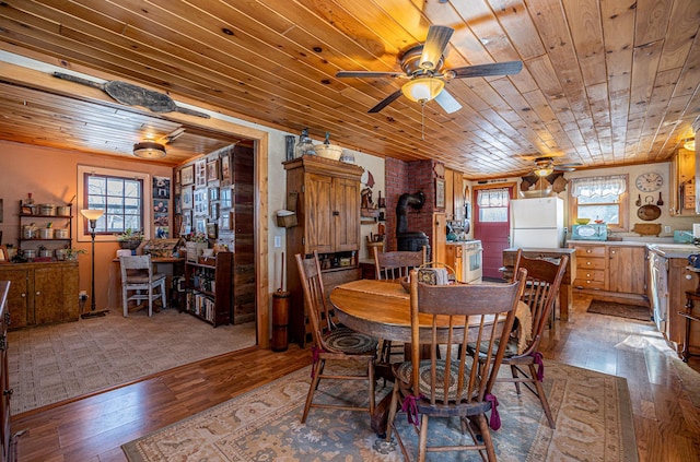 dining room with a ceiling fan, hardwood / wood-style floors, a wealth of natural light, a wood stove, and wooden ceiling
