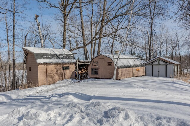 yard layered in snow featuring an outdoor structure, a garage, and a shed
