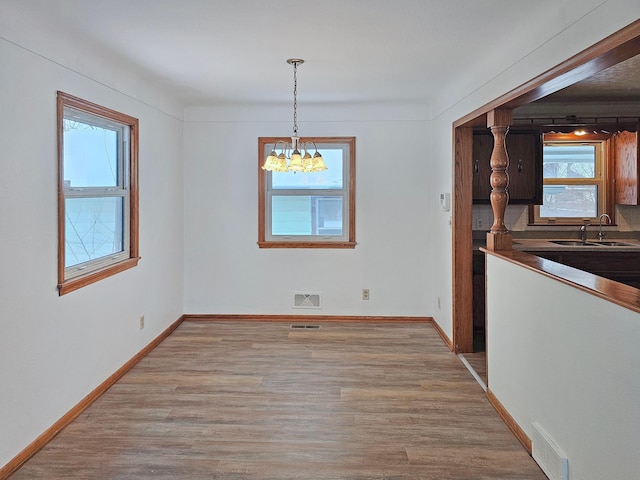 unfurnished dining area with sink, a chandelier, and light hardwood / wood-style floors