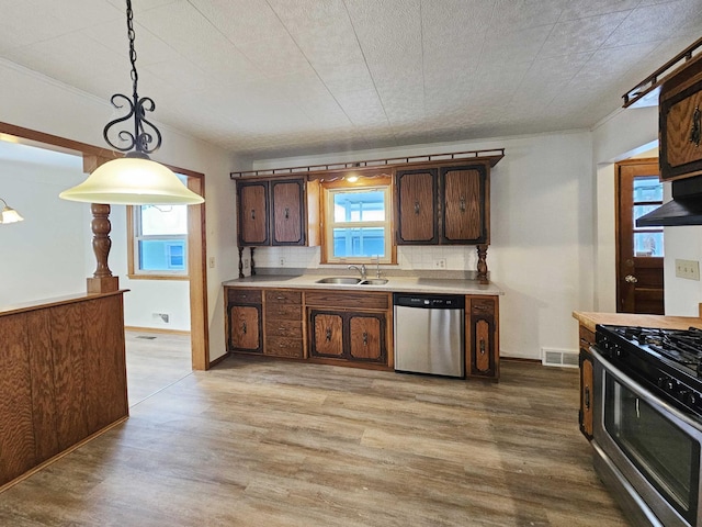 kitchen featuring pendant lighting, sink, decorative backsplash, stainless steel appliances, and light wood-type flooring