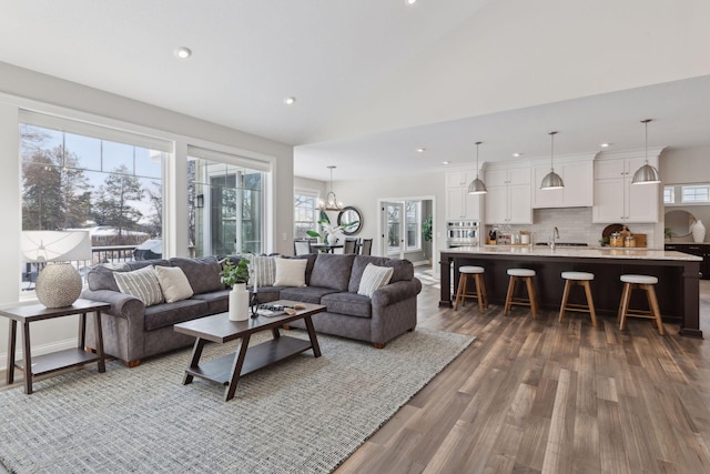 living room with a notable chandelier, wood-type flooring, high vaulted ceiling, and sink