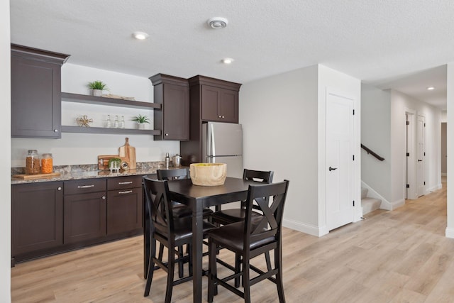 kitchen with light hardwood / wood-style flooring, stainless steel refrigerator, dark brown cabinets, light stone counters, and a textured ceiling