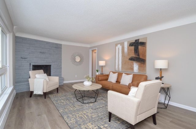 living room with hardwood / wood-style flooring, a stone fireplace, and a textured ceiling