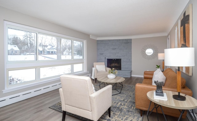 living room featuring a baseboard heating unit, hardwood / wood-style flooring, and a stone fireplace