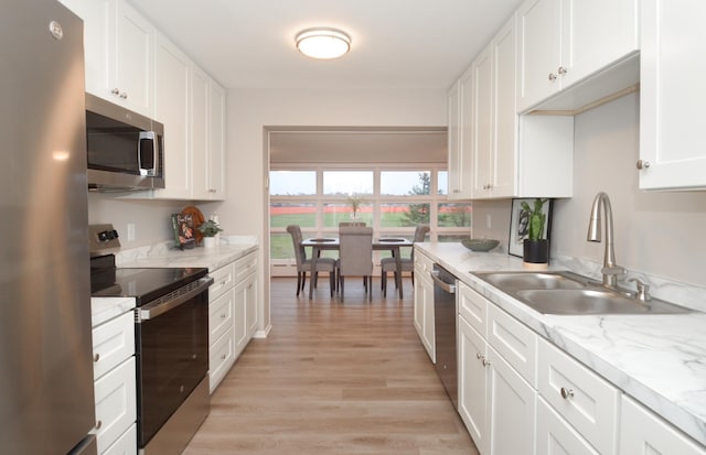 kitchen with light stone countertops, light wood-style flooring, appliances with stainless steel finishes, a sink, and white cabinetry