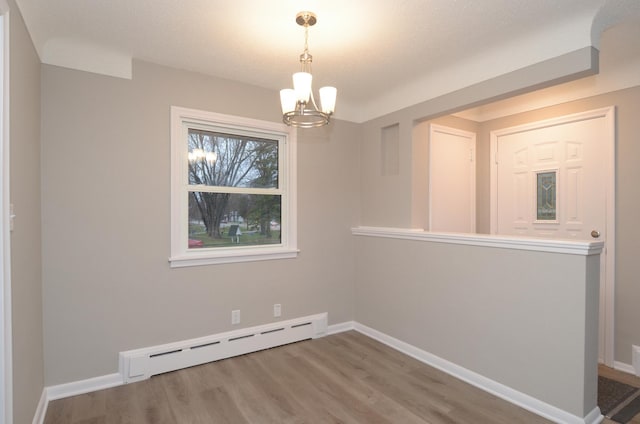 spare room featuring baseboards, wood finished floors, a baseboard heating unit, and an inviting chandelier