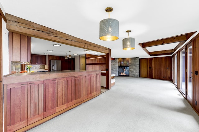 kitchen featuring a stone fireplace, wooden walls, light carpet, open floor plan, and stainless steel refrigerator with ice dispenser