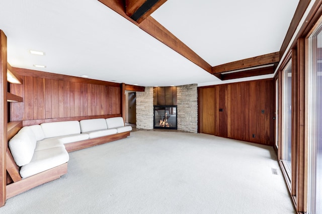 unfurnished living room with wooden walls, visible vents, carpet flooring, a stone fireplace, and beam ceiling