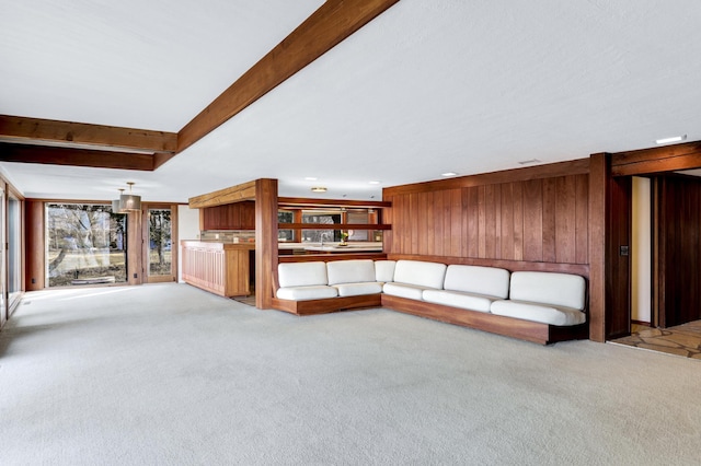 unfurnished living room featuring carpet, wooden walls, and beam ceiling