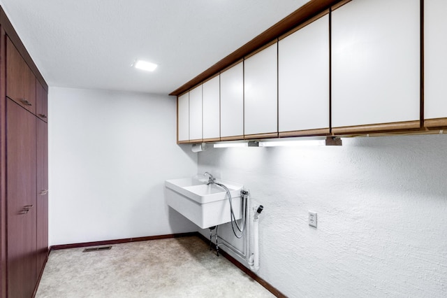 laundry area with light colored carpet, a sink, visible vents, baseboards, and cabinet space