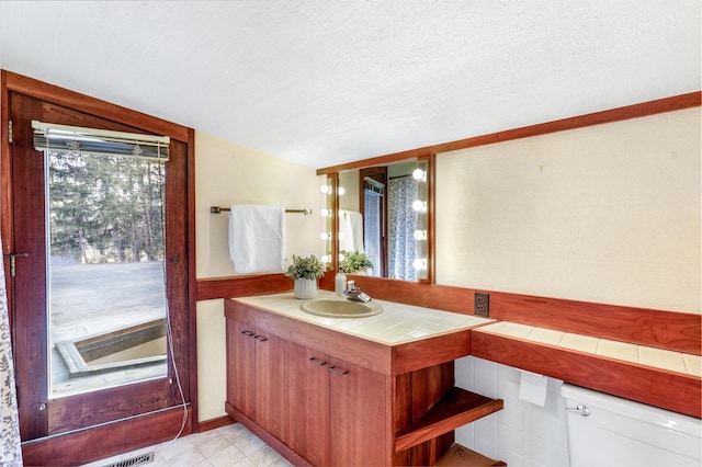 kitchen with a textured ceiling, a sink, vaulted ceiling, tile counters, and open shelves