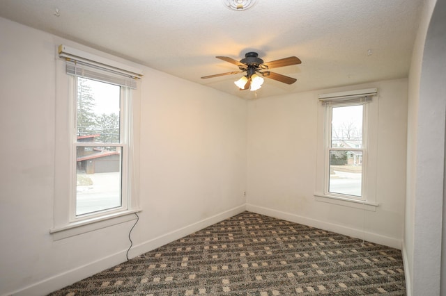 carpeted empty room with ceiling fan, a wealth of natural light, and a textured ceiling