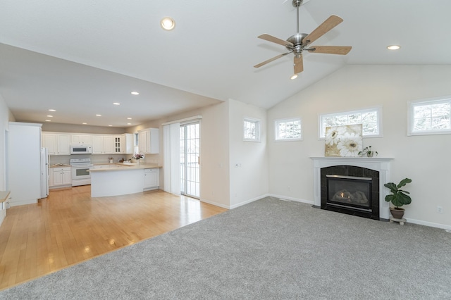 unfurnished living room with ceiling fan, vaulted ceiling, light carpet, and a tiled fireplace