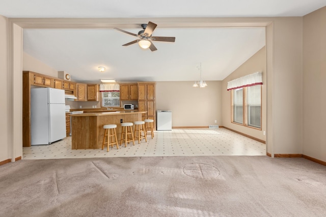 kitchen with a kitchen bar, decorative light fixtures, vaulted ceiling, white fridge, and light colored carpet