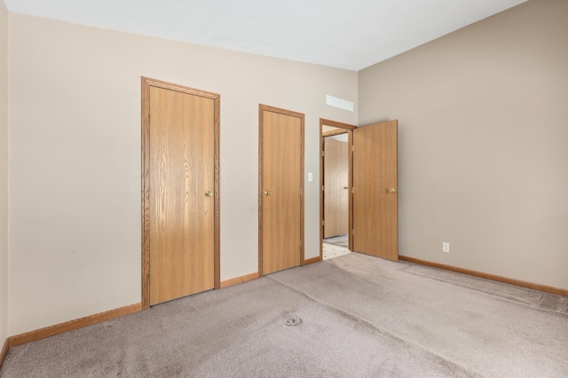 unfurnished bedroom with lofted ceiling, two closets, and light colored carpet