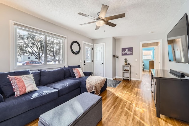 living room with ceiling fan, light hardwood / wood-style flooring, a textured ceiling, and plenty of natural light