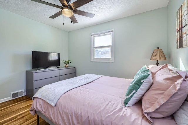 bedroom featuring ceiling fan, hardwood / wood-style floors, and a textured ceiling