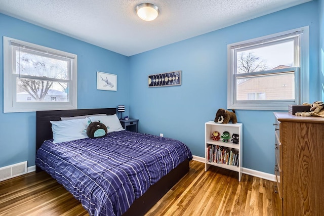 bedroom featuring multiple windows, dark wood-type flooring, and a textured ceiling