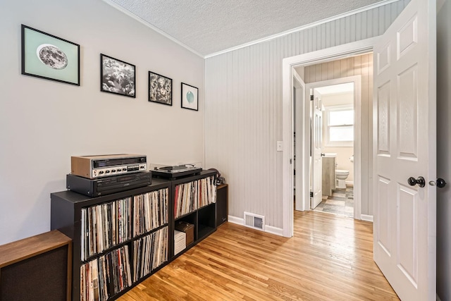 hallway with crown molding, a textured ceiling, and light wood-type flooring