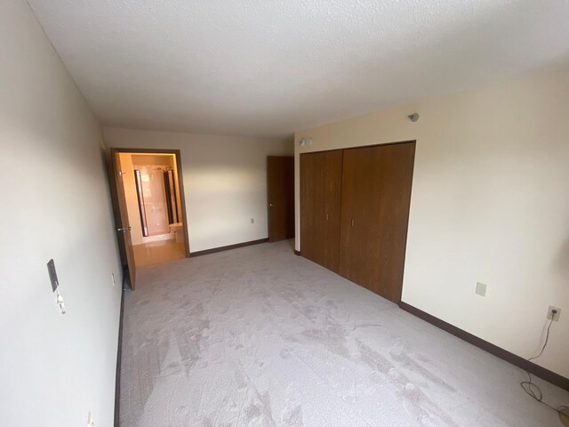 unfurnished bedroom featuring light carpet, ensuite bath, a closet, and a textured ceiling