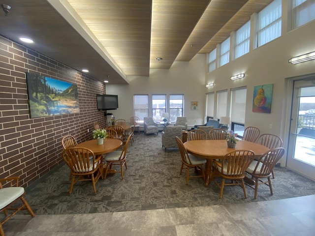 dining space with wood ceiling, a towering ceiling, brick wall, and plenty of natural light