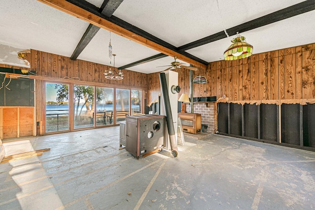 unfurnished living room featuring a wood stove, wood walls, a textured ceiling, and beam ceiling