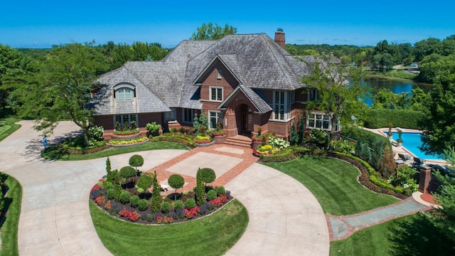 view of front of home featuring brick siding, a chimney, concrete driveway, a water view, and a front lawn