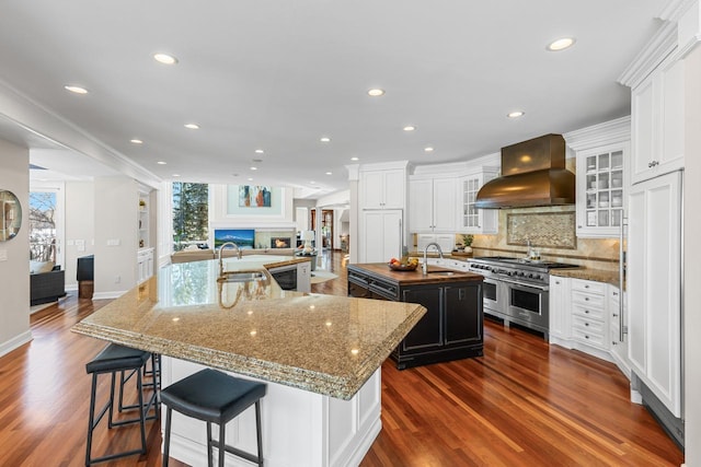 kitchen with range with two ovens, a spacious island, wall chimney exhaust hood, open floor plan, and a fireplace