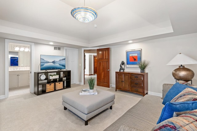 living area featuring light carpet, a tray ceiling, and baseboards