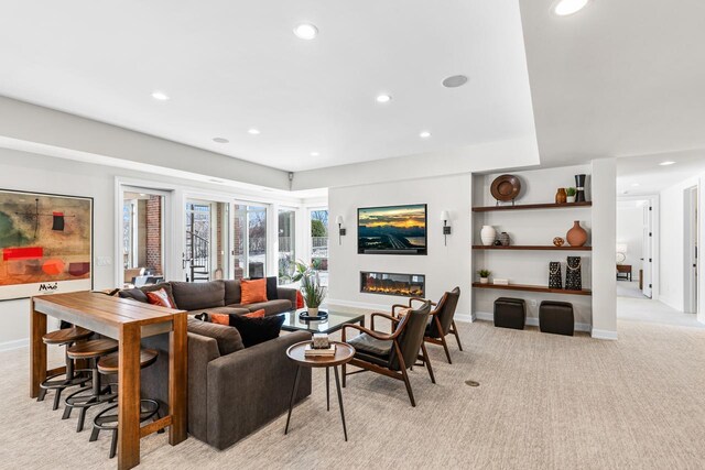 living area featuring light carpet, baseboards, a glass covered fireplace, and recessed lighting