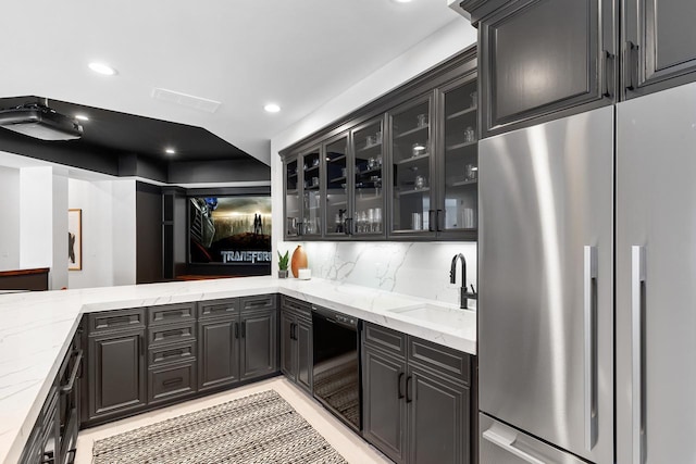 kitchen featuring a sink, decorative backsplash, light stone countertops, stainless steel fridge, and glass insert cabinets