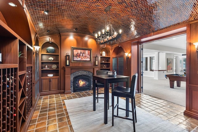 wine cellar with brick ceiling, a warm lit fireplace, built in shelves, and vaulted ceiling