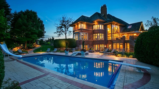 outdoor pool with a diving board, a water slide, and a patio