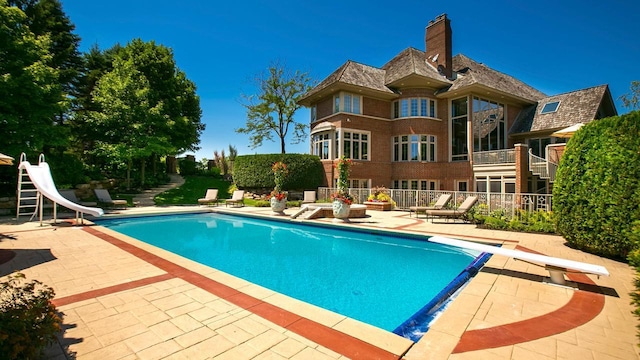 outdoor pool with a water slide, a patio, fence, and a diving board