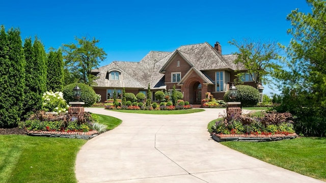 view of front of property with a chimney, curved driveway, and a front yard