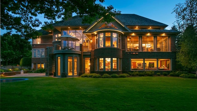 rear view of property featuring a sunroom, brick siding, a lawn, and a balcony