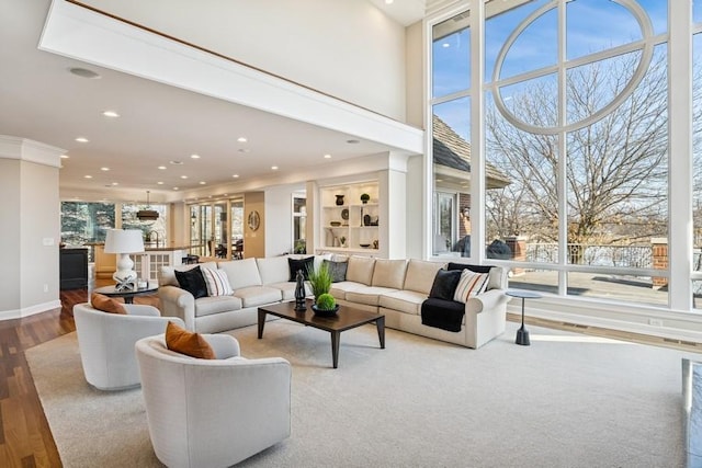 living area with baseboards, wood finished floors, a high ceiling, built in shelves, and recessed lighting