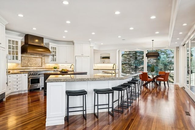 kitchen with a large island, custom range hood, dark wood-type flooring, high end stainless steel range oven, and a sink